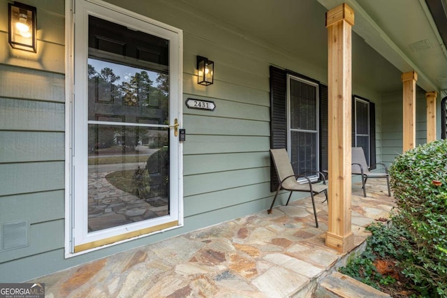 view of exterior entry with visible vents and a porch