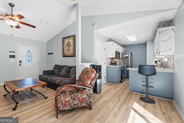 living area with baseboards, light wood-style floors, a ceiling fan, and vaulted ceiling