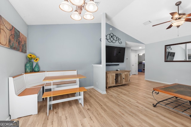 dining space featuring visible vents, light wood-style flooring, ceiling fan with notable chandelier, baseboards, and vaulted ceiling