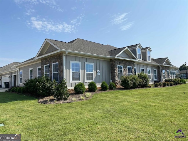 view of front facade with a front lawn, stone siding, board and batten siding, an attached garage, and a shingled roof