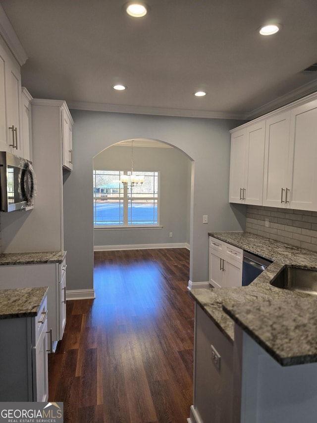 kitchen featuring a notable chandelier, backsplash, stainless steel appliances, arched walkways, and light stone countertops