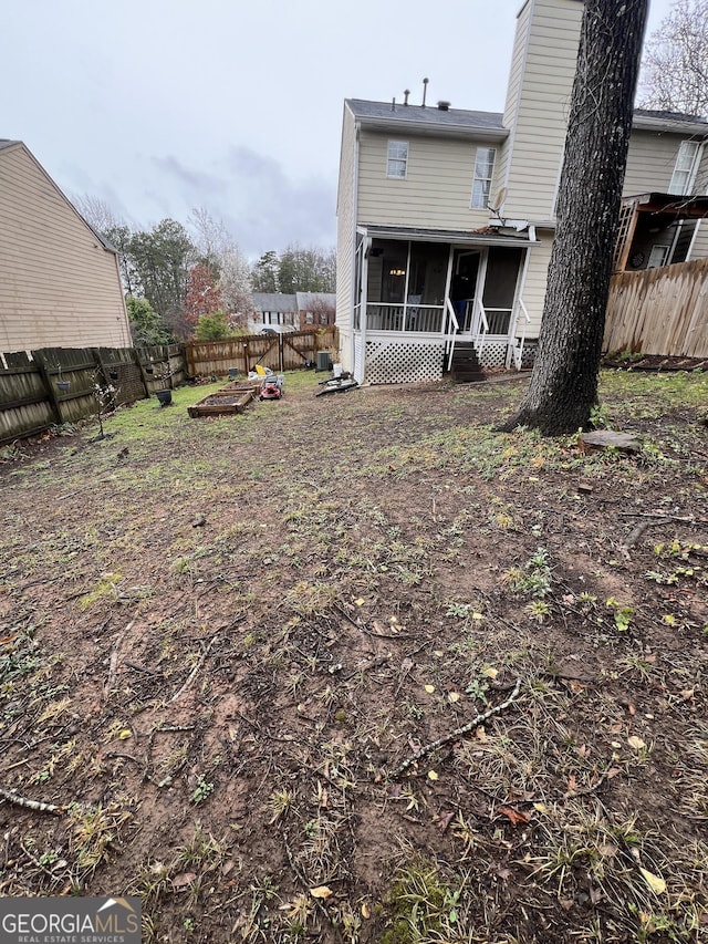 back of house with a fenced backyard, a sunroom, and a chimney