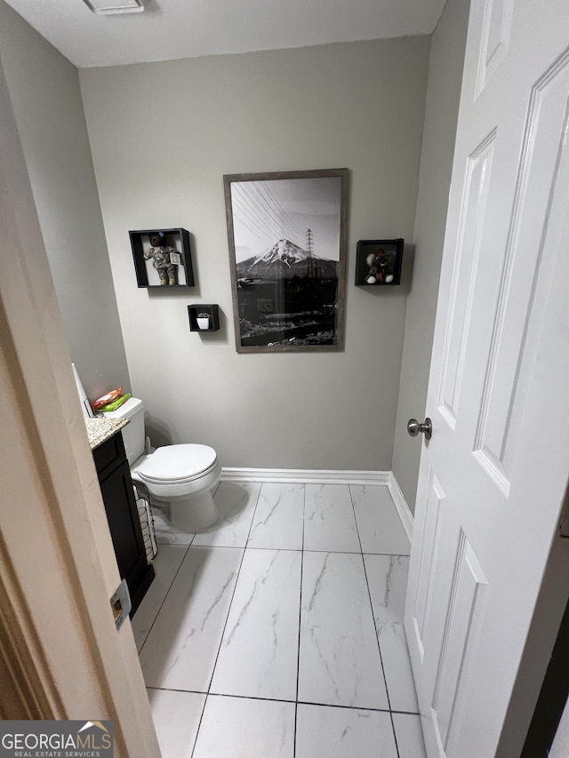 half bath featuring marble finish floor, toilet, vanity, and baseboards