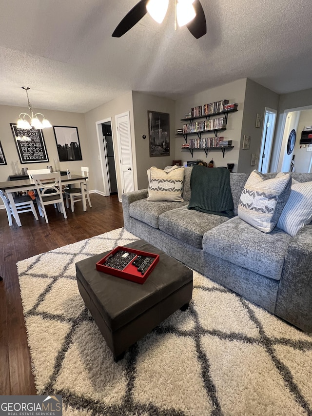 living area with ceiling fan with notable chandelier, wood finished floors, and a textured ceiling