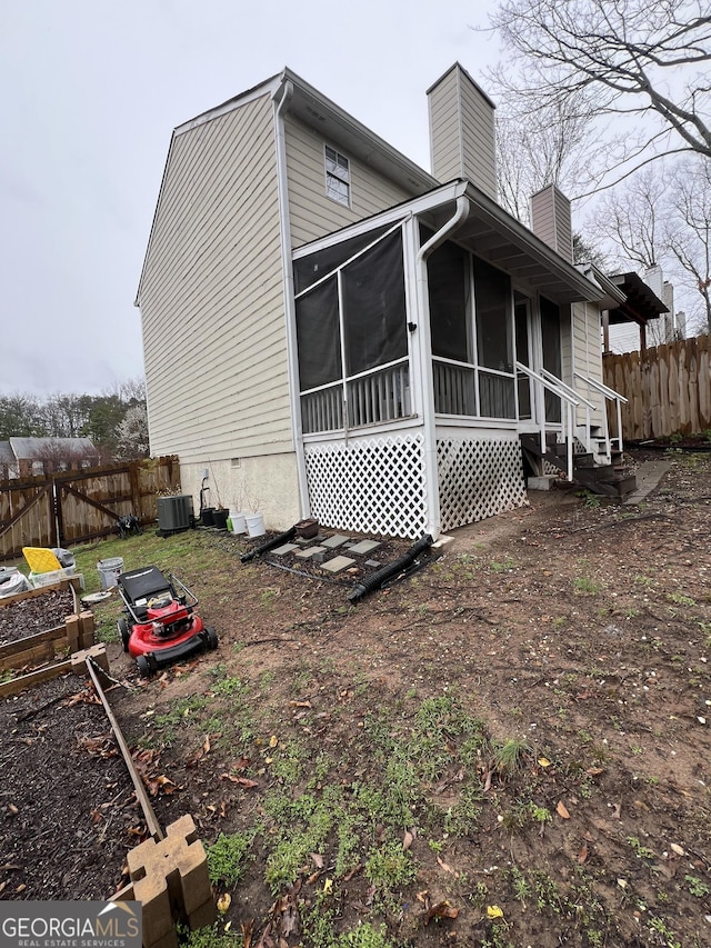 view of side of property featuring a chimney, a sunroom, central AC, and fence