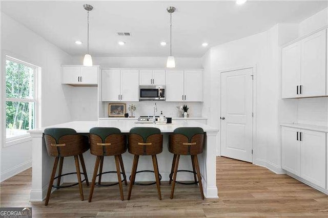 kitchen featuring white cabinetry, stainless steel microwave, and decorative backsplash