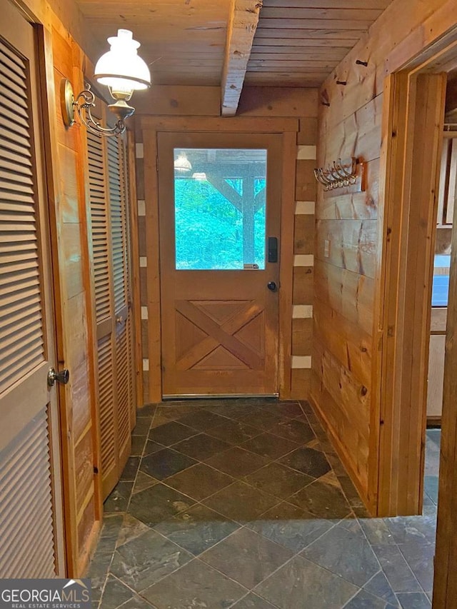 doorway with stone tile flooring, beamed ceiling, wooden ceiling, and wood walls