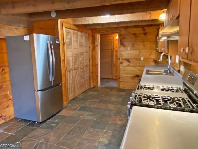 kitchen with wooden walls, under cabinet range hood, stone finish floor, stainless steel appliances, and a sink