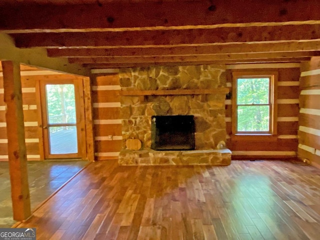 unfurnished living room with a stone fireplace, beam ceiling, and wood finished floors