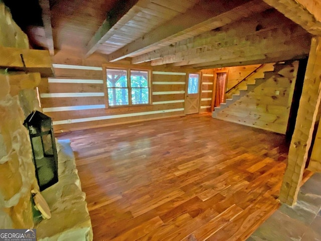 unfurnished living room featuring stairway, beam ceiling, wooden walls, and wood finished floors