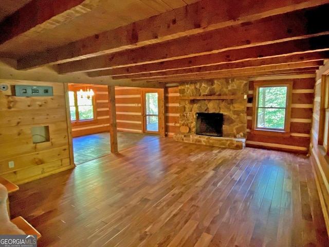 unfurnished living room featuring beam ceiling, a stone fireplace, a healthy amount of sunlight, and wood finished floors