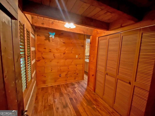 unfurnished bedroom with wood finished floors, a closet, wood walls, wooden ceiling, and beamed ceiling