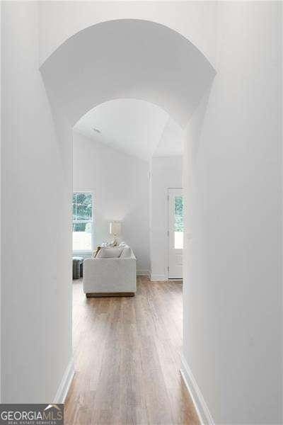 hall featuring baseboards, arched walkways, wood finished floors, and vaulted ceiling