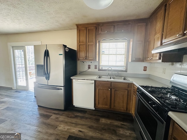 kitchen featuring a sink, backsplash, under cabinet range hood, appliances with stainless steel finishes, and dark wood-style flooring