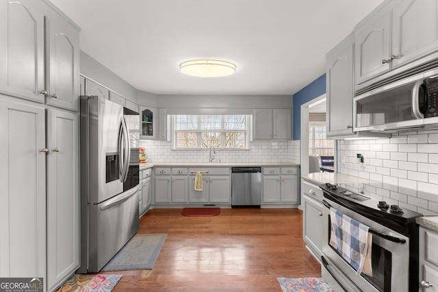 kitchen featuring tasteful backsplash, light countertops, appliances with stainless steel finishes, wood-type flooring, and a sink