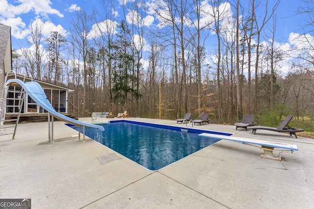 pool with a patio, a diving board, and a water slide