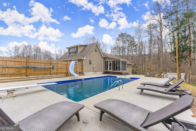 view of swimming pool featuring fence, a water slide, a sunroom, a diving board, and a patio area