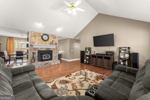 living area with high vaulted ceiling, ceiling fan with notable chandelier, wood finished floors, a stone fireplace, and baseboards