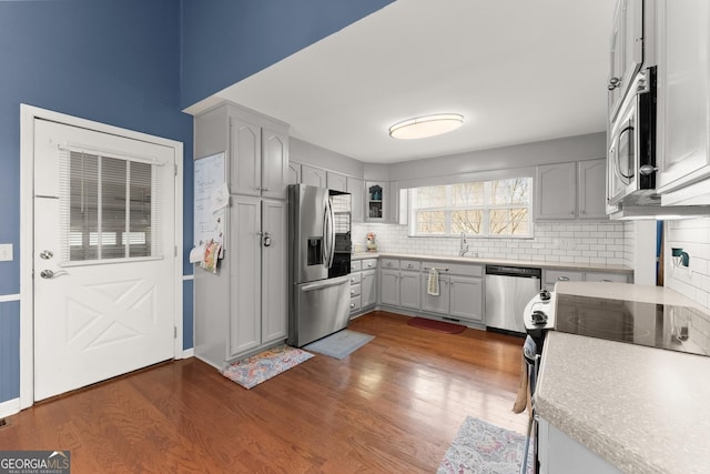 kitchen featuring a sink, tasteful backsplash, stainless steel appliances, light countertops, and dark wood-style flooring