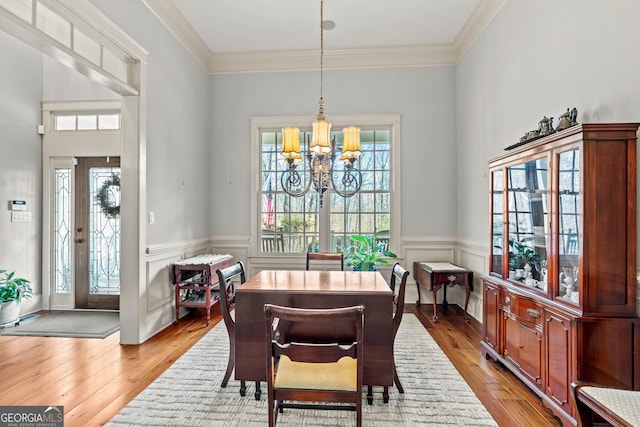 dining room featuring light wood finished floors, a wainscoted wall, an inviting chandelier, and ornamental molding