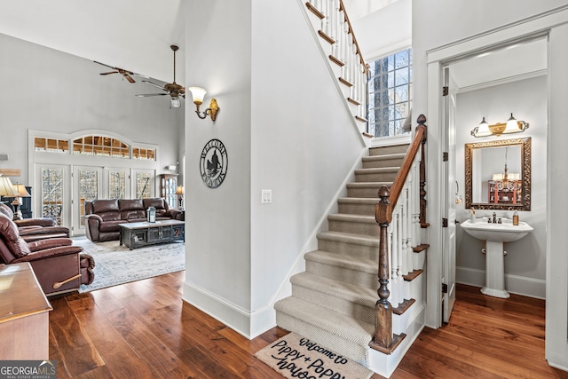 staircase featuring hardwood / wood-style flooring, a high ceiling, a ceiling fan, and baseboards