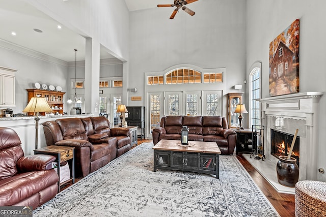 living room featuring dark wood-style floors, a premium fireplace, a high ceiling, ornamental molding, and ceiling fan