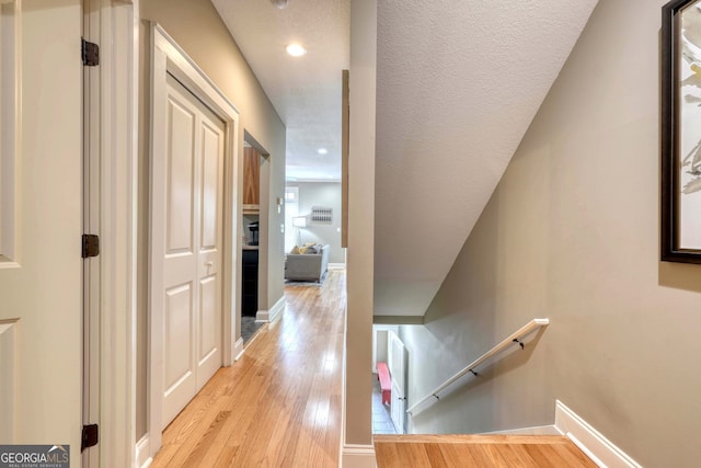 hallway with an upstairs landing, recessed lighting, light wood-type flooring, and baseboards