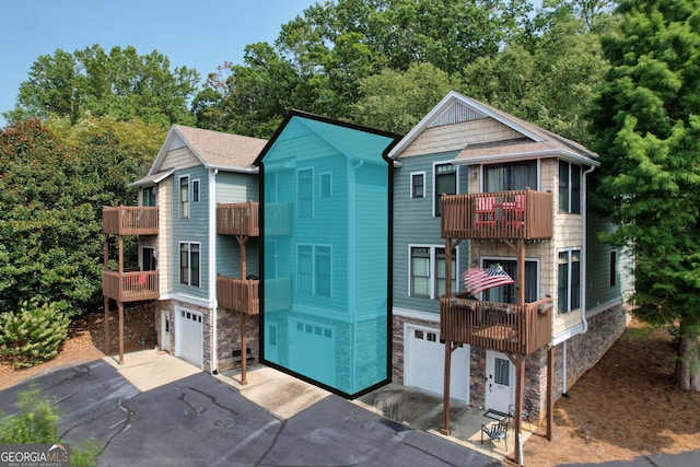 view of front of house featuring stone siding, driveway, a balcony, and an attached garage