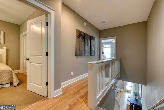 hallway featuring an upstairs landing, baseboards, and light wood finished floors