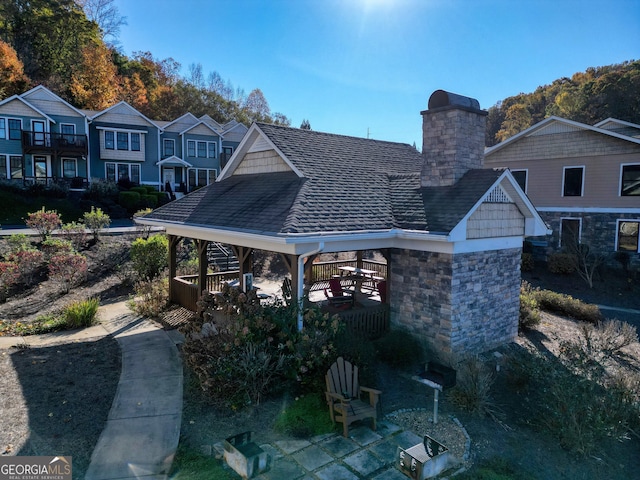 back of house with a gazebo, stone siding, a chimney, and a shingled roof