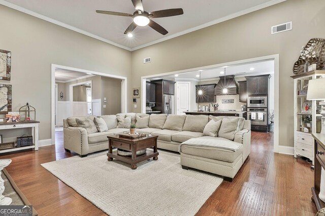 living room featuring crown molding, visible vents, dark wood-style flooring, and ceiling fan