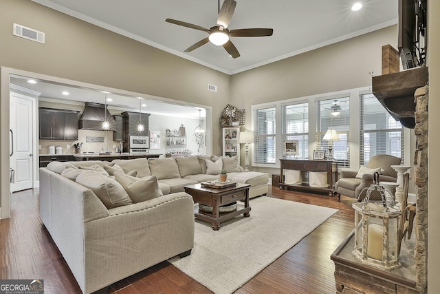 living area featuring dark wood-type flooring, ornamental molding, visible vents, and ceiling fan