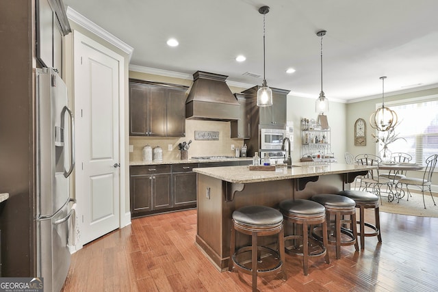 kitchen with custom exhaust hood, a breakfast bar area, appliances with stainless steel finishes, and dark brown cabinetry