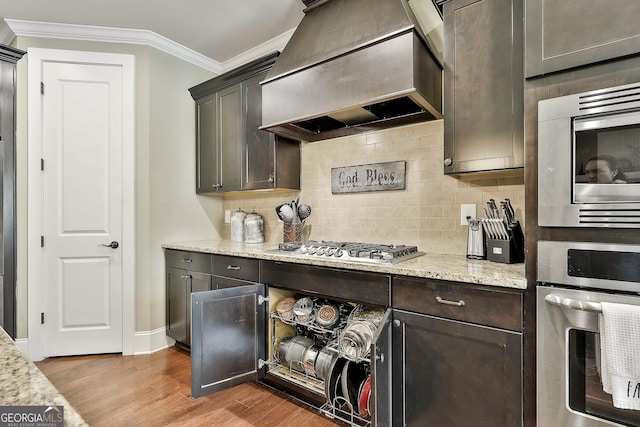 kitchen featuring custom range hood, wood finished floors, appliances with stainless steel finishes, crown molding, and decorative backsplash