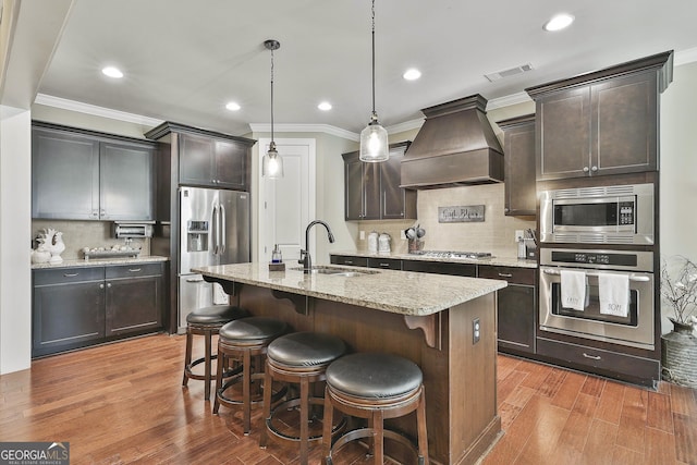 kitchen with visible vents, light wood finished floors, a sink, stainless steel appliances, and custom range hood