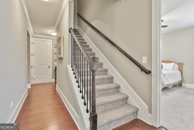 stairs with baseboards, wood finished floors, and crown molding