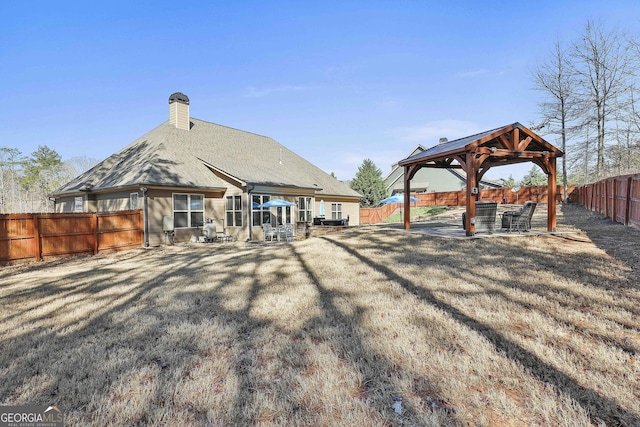 rear view of house with a fenced backyard, a gazebo, a yard, a chimney, and a patio area