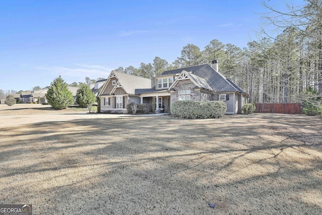 view of front of property featuring a front yard, fence, a shingled roof, a chimney, and stone siding