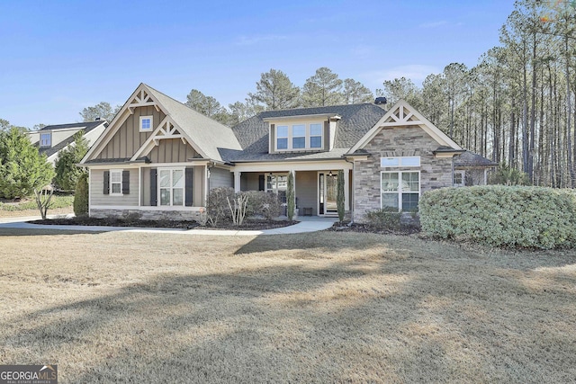 craftsman-style home featuring board and batten siding, a front lawn, stone siding, and roof with shingles