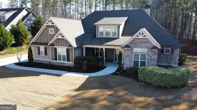 craftsman-style home featuring stone siding, board and batten siding, a chimney, and roof with shingles