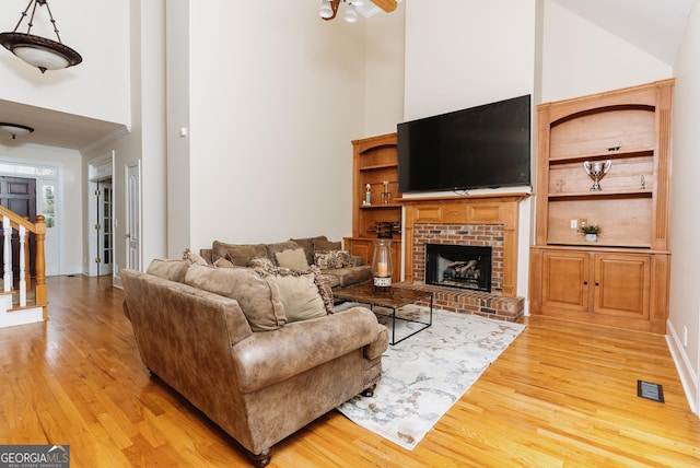 living room with visible vents, a towering ceiling, a fireplace, and light wood finished floors