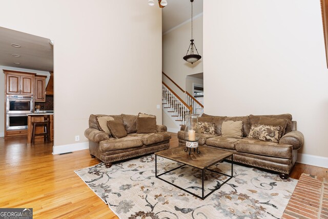 living area with light wood-type flooring, visible vents, stairway, crown molding, and baseboards