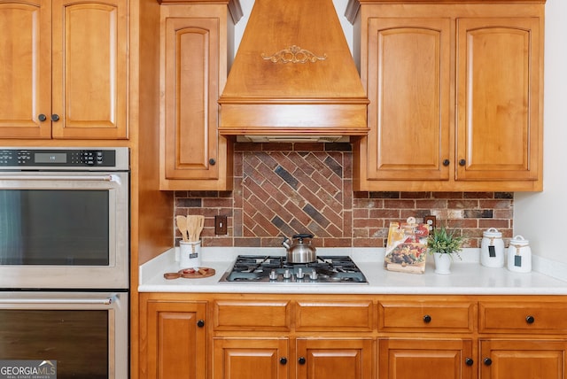 kitchen featuring decorative backsplash, appliances with stainless steel finishes, light countertops, and premium range hood