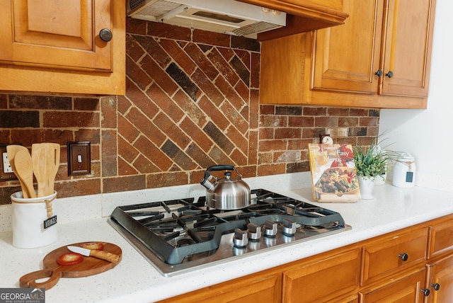 kitchen with backsplash, brown cabinetry, light countertops, extractor fan, and stainless steel gas cooktop