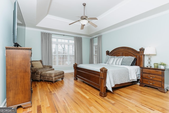 bedroom featuring a ceiling fan, light wood-type flooring, a tray ceiling, and ornamental molding