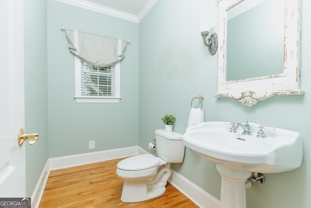 half bath featuring toilet, wood finished floors, baseboards, and ornamental molding