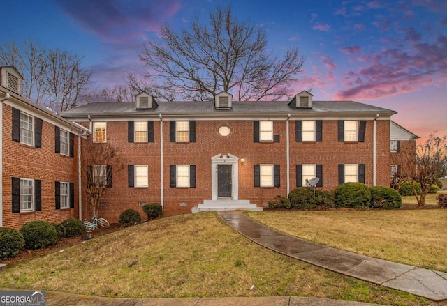 colonial inspired home with brick siding and a lawn