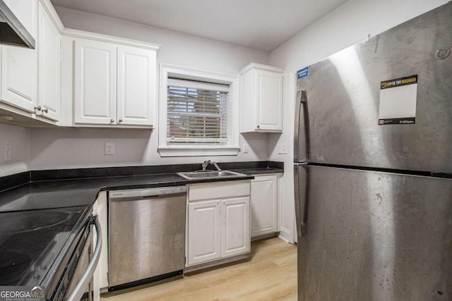 kitchen featuring light wood finished floors, white cabinets, stainless steel appliances, wall chimney exhaust hood, and a sink