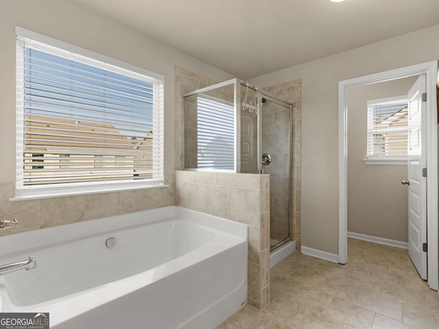 bathroom with baseboards, a garden tub, a healthy amount of sunlight, and a shower stall