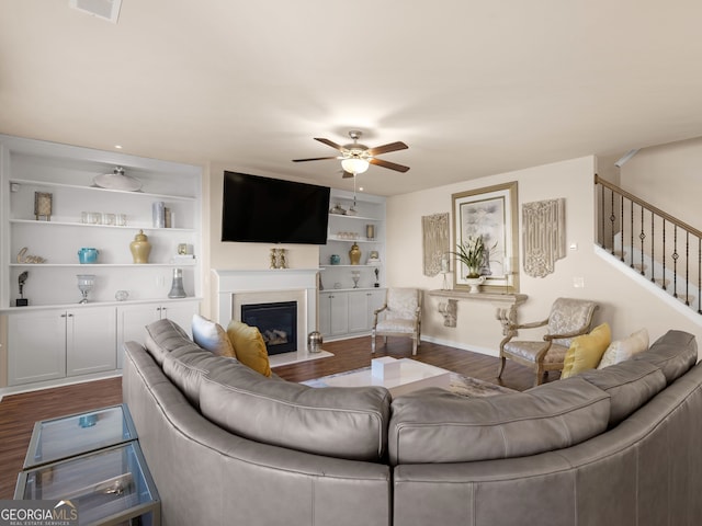 living area featuring dark wood-type flooring, stairway, built in shelves, and a ceiling fan